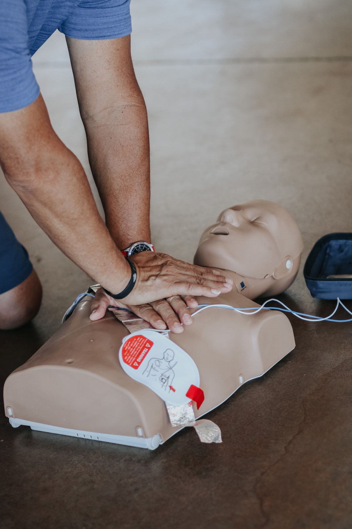 Mains effectuant des compressions thoraciques sur un mannequin de formation, à côté d'un défibrillateur