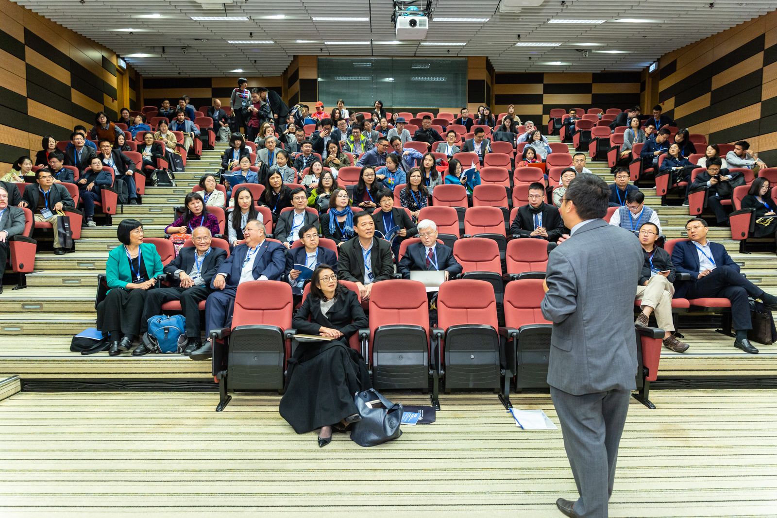 Un homme s'exprime debout devant un public assis dans un auditorium lors d'une conférence professionnelle