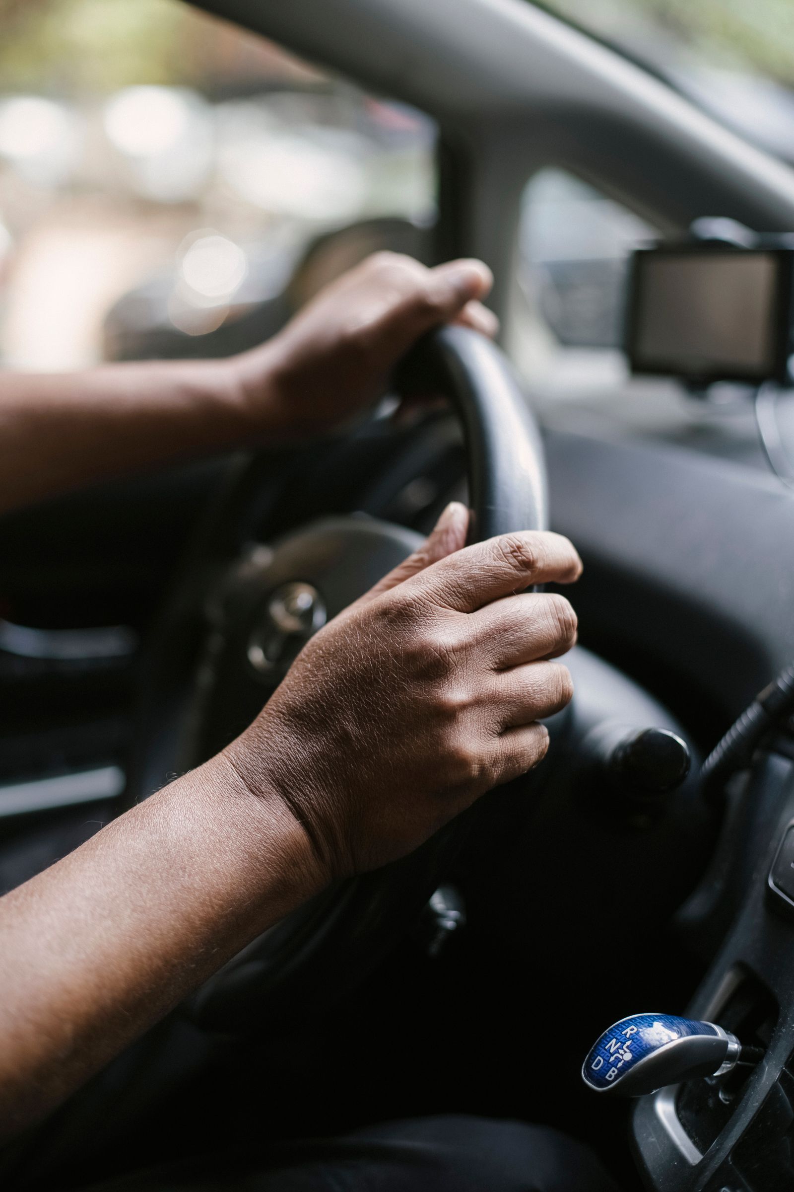 Gros plan sur les mains d'un conducteur au volant, avec un GPS visible sur le tableau de bord