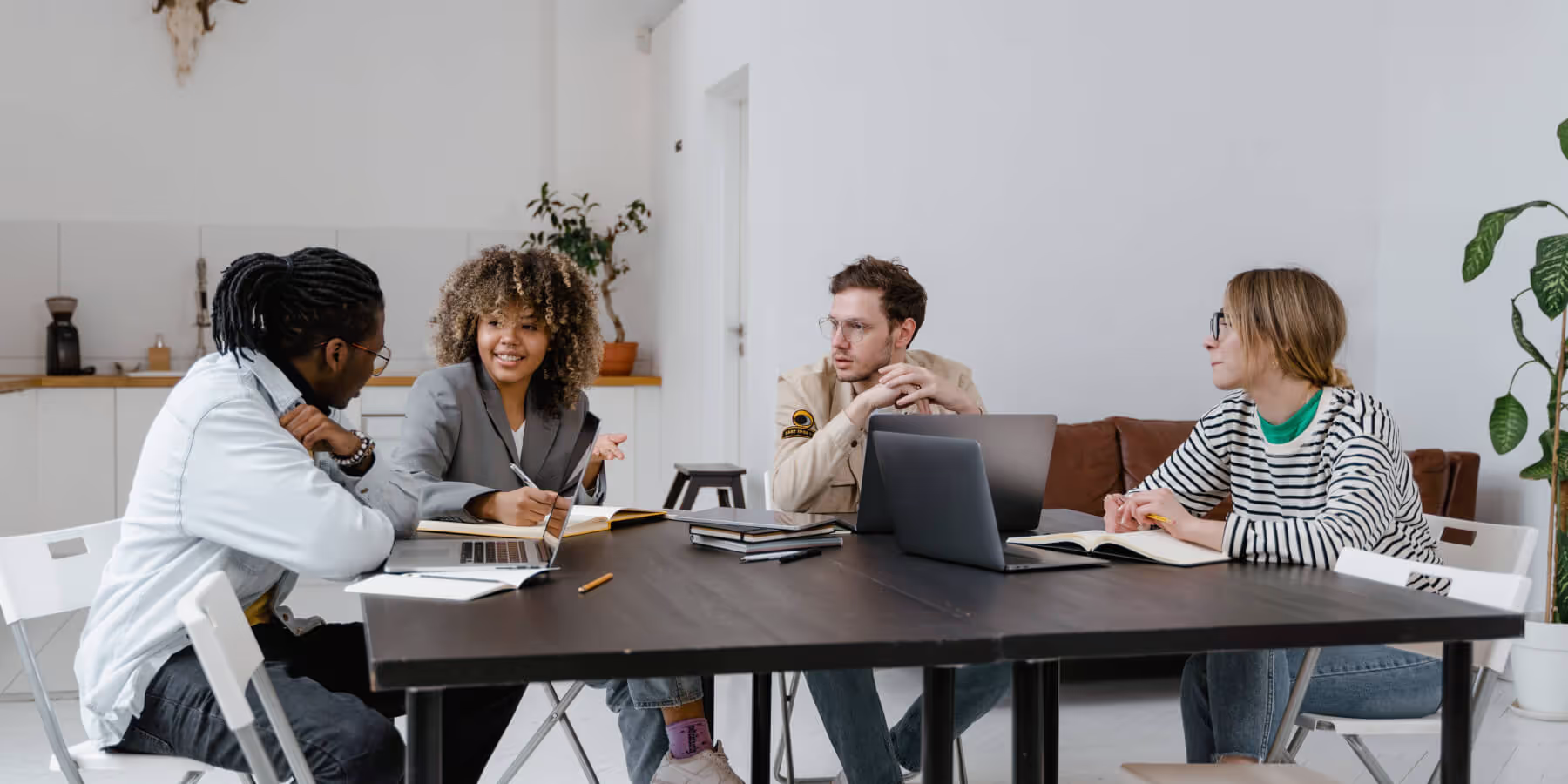 Quatre collègues en réunion de travail autour d'une grande table, l'une d'elles prend des notes