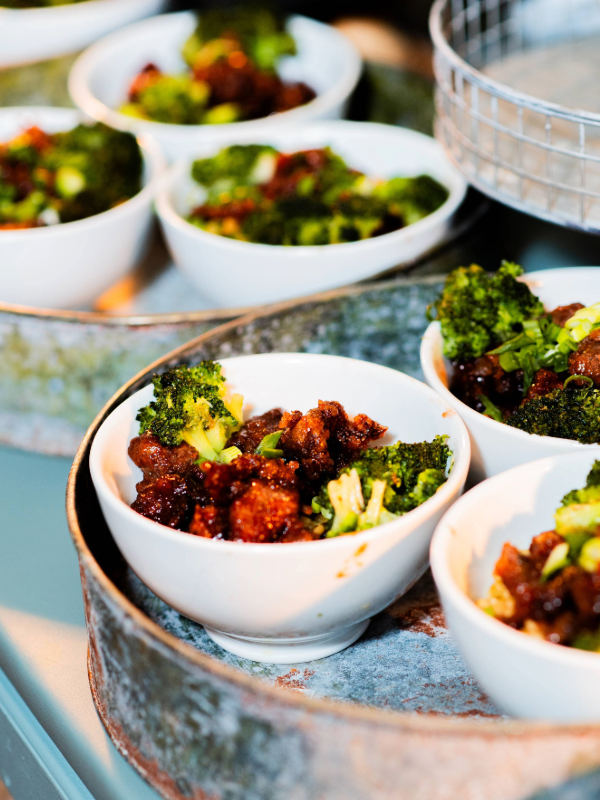 White bowls filled with broccoli and seasoned meat placed on a rustic metal tray.