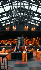 Cozy bar interior with a large chandelier, wooden tables, stools, and a central black circular seating area with cushions.