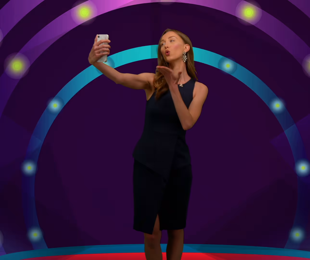 Woman in a black sleeveless dress taking a selfie and blowing a kiss against a dark background with colorful circular light patterns.