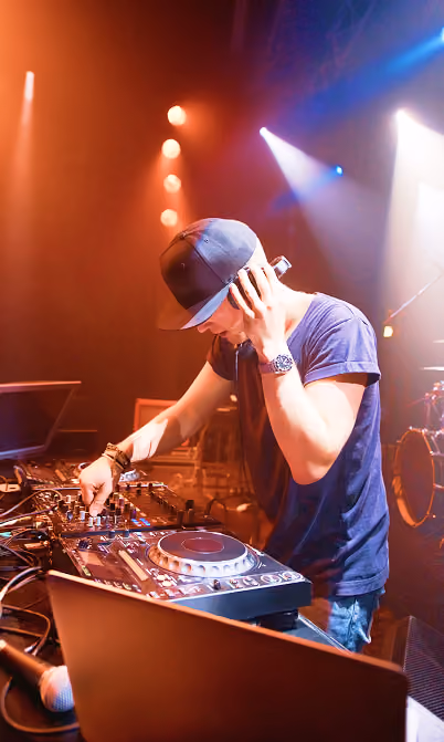 DJ wearing a cap and headphones mixing music on a DJ controller under stage lights.