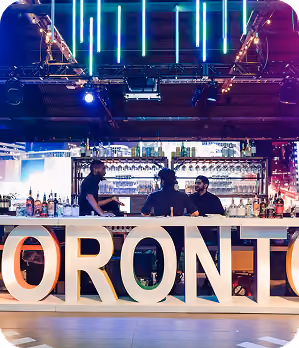 Bar scene with three bartenders behind large illuminated letters spelling TORONTO.