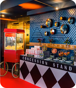 Concession stand with popcorn machine and snacks against a patterned blue wall with round mirrors.