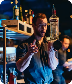 Bartender spinning a bottle of Smirnoff vodka on his finger behind the bar at night.