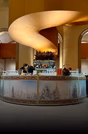 Curved golden chandelier above bar counter with frosted glass panels showing snowy trees.