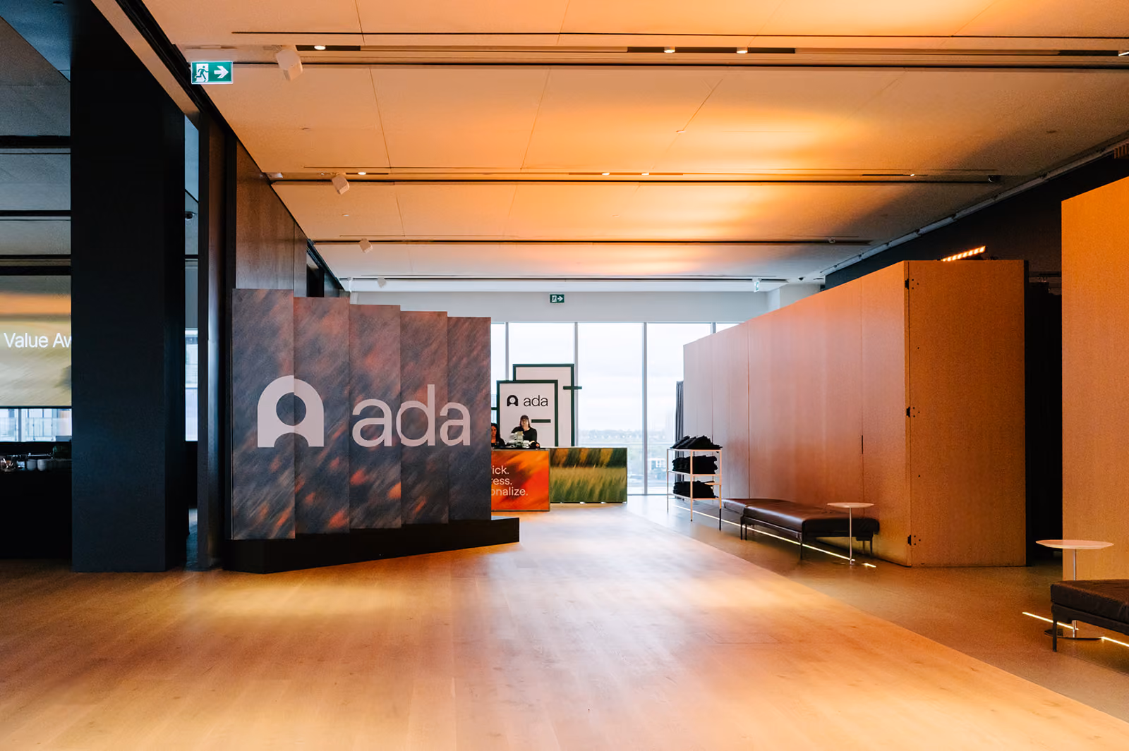 Modern office lobby with large ada sign, light wood floor, benches, and a reception desk.