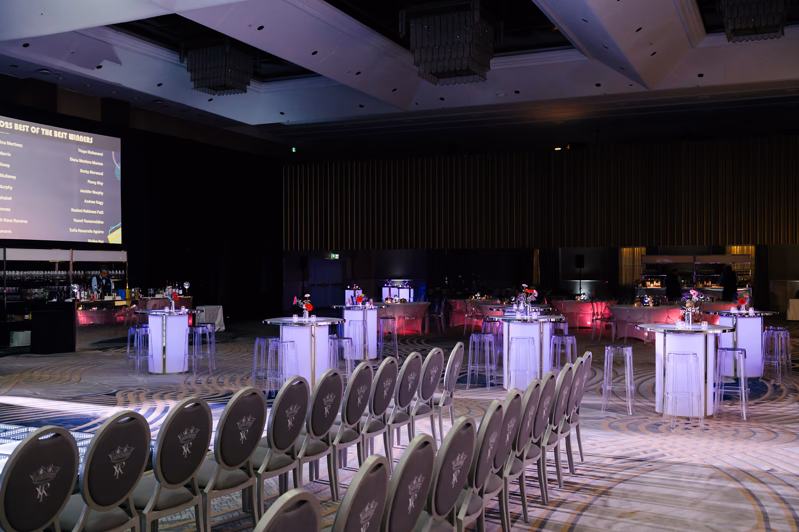Empty event space with rows of chairs facing lit cocktail tables with flower centerpieces.