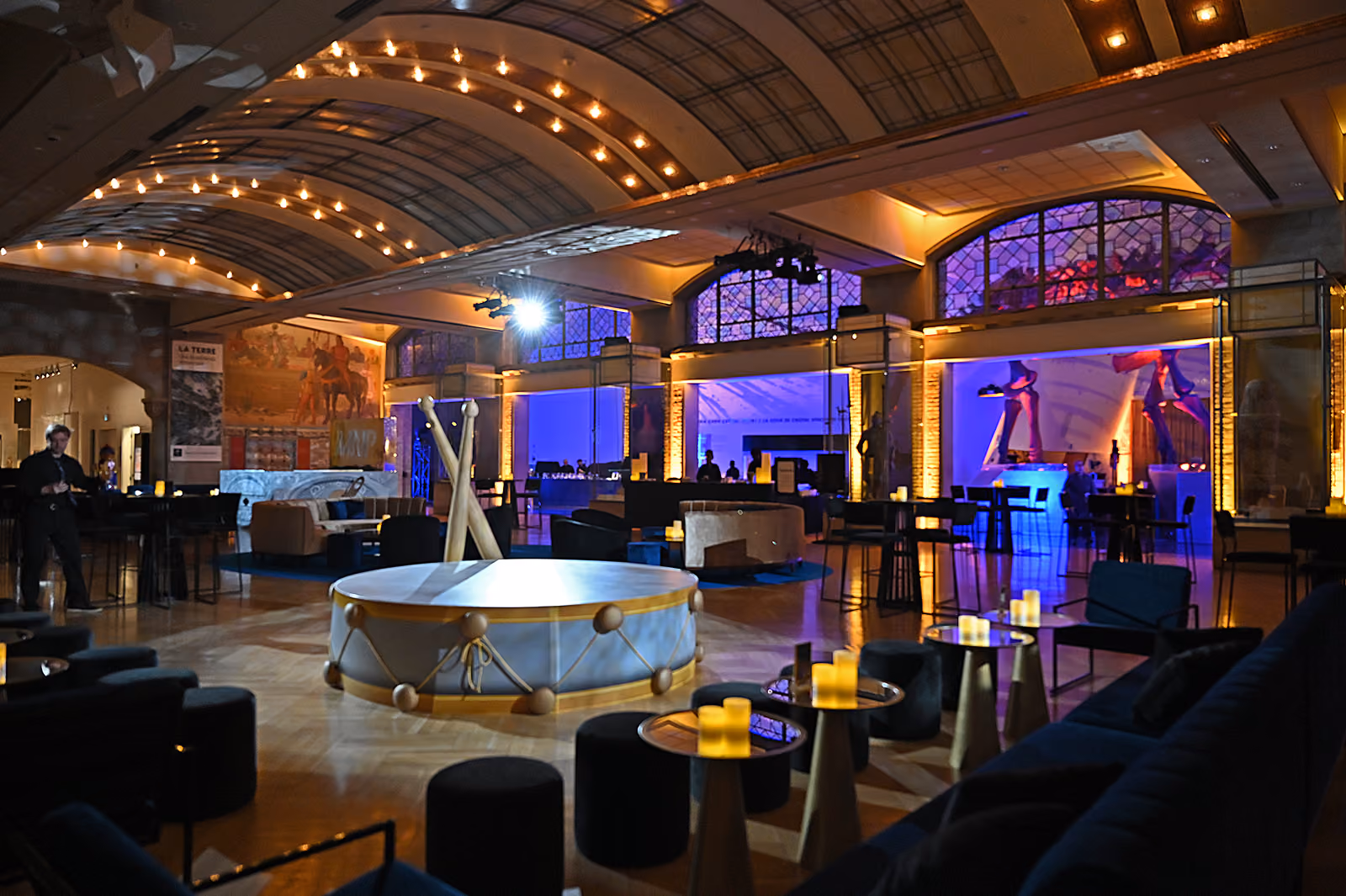 Large drum centerpiece in dimly lit event hall with lounge seating and mood lighting.