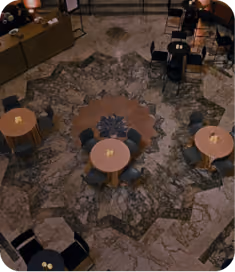 Overhead view of a seating area with round tables and chairs arranged on a decorative marble floor with a central design, in a dimly lit environment.