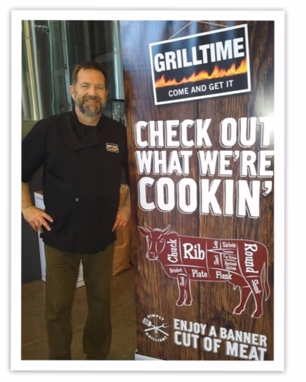 Grillmaster standing next to a sign