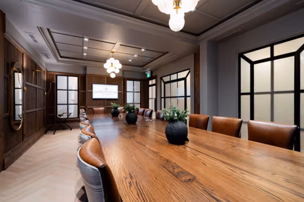 The Dominion meeting room at The Dorchester Hotel features a long, elegant wooden table, plush leather chairs, and stylish lighting. The room offers a sophisticated atmosphere perfect for executive meetings or private gatherings