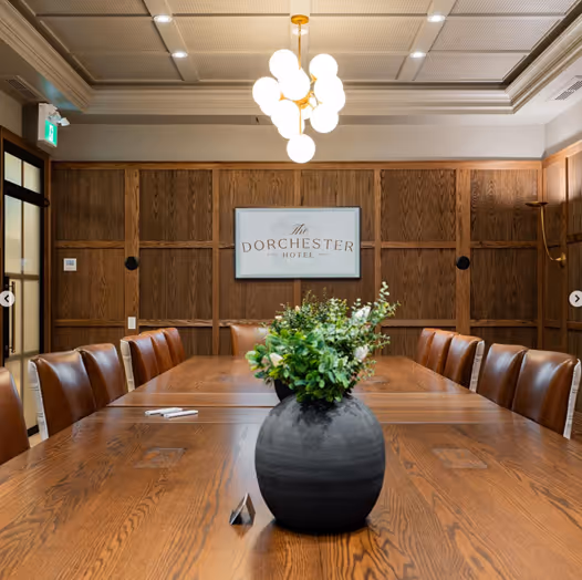 The Dominion meeting room at The Dorchester Hotel offers a sophisticated space with rich wood paneling, a large polished conference table, and elegant lighting. Ideal for professional gatherings, the room combines style and functionality in a refined setting