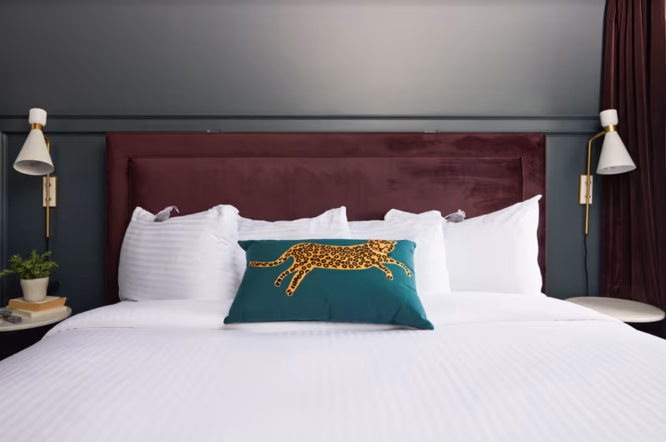 This stylish bedroom features a bold maroon headboard, crisp white linens, and a playful leopard-themed accent pillow