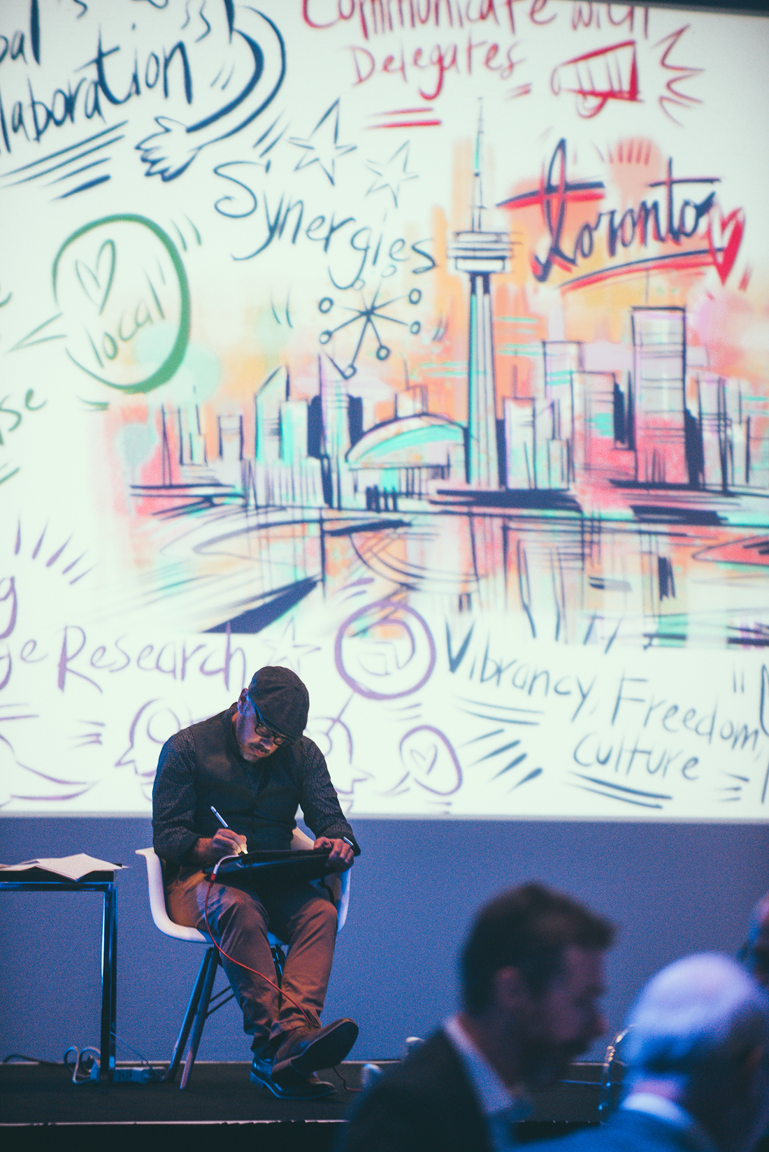 a moment of live graphic recording or scribing during a corporate event or presentation. A person is creating real-time illustrations on a digital tablet, which are simultaneously projected onto a large screen behind them.