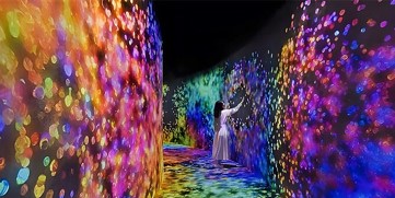 An immersive digital art installation by teamLab featuring vibrant, multi-colored light patterns.