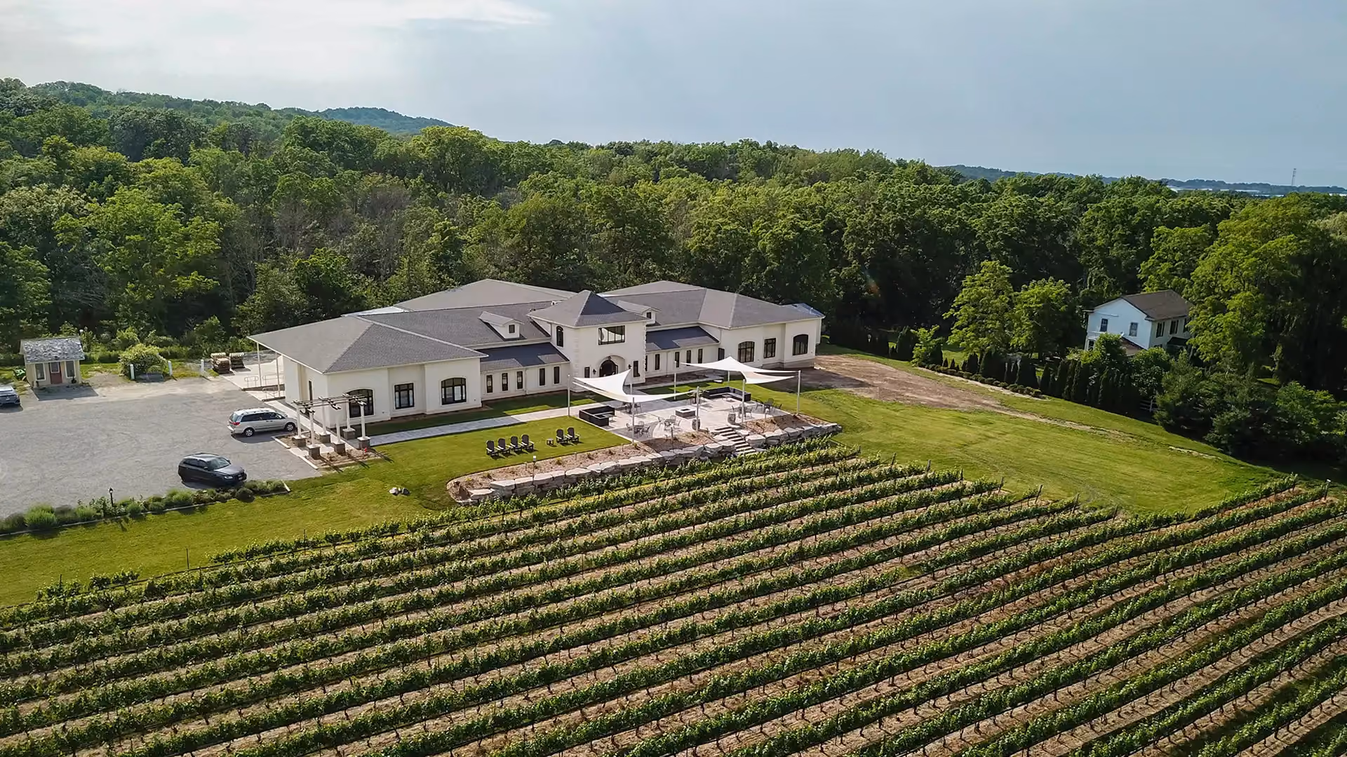 Modern vineyard estate with central building, patio shade sails, and rows of grapevines among rolling hills