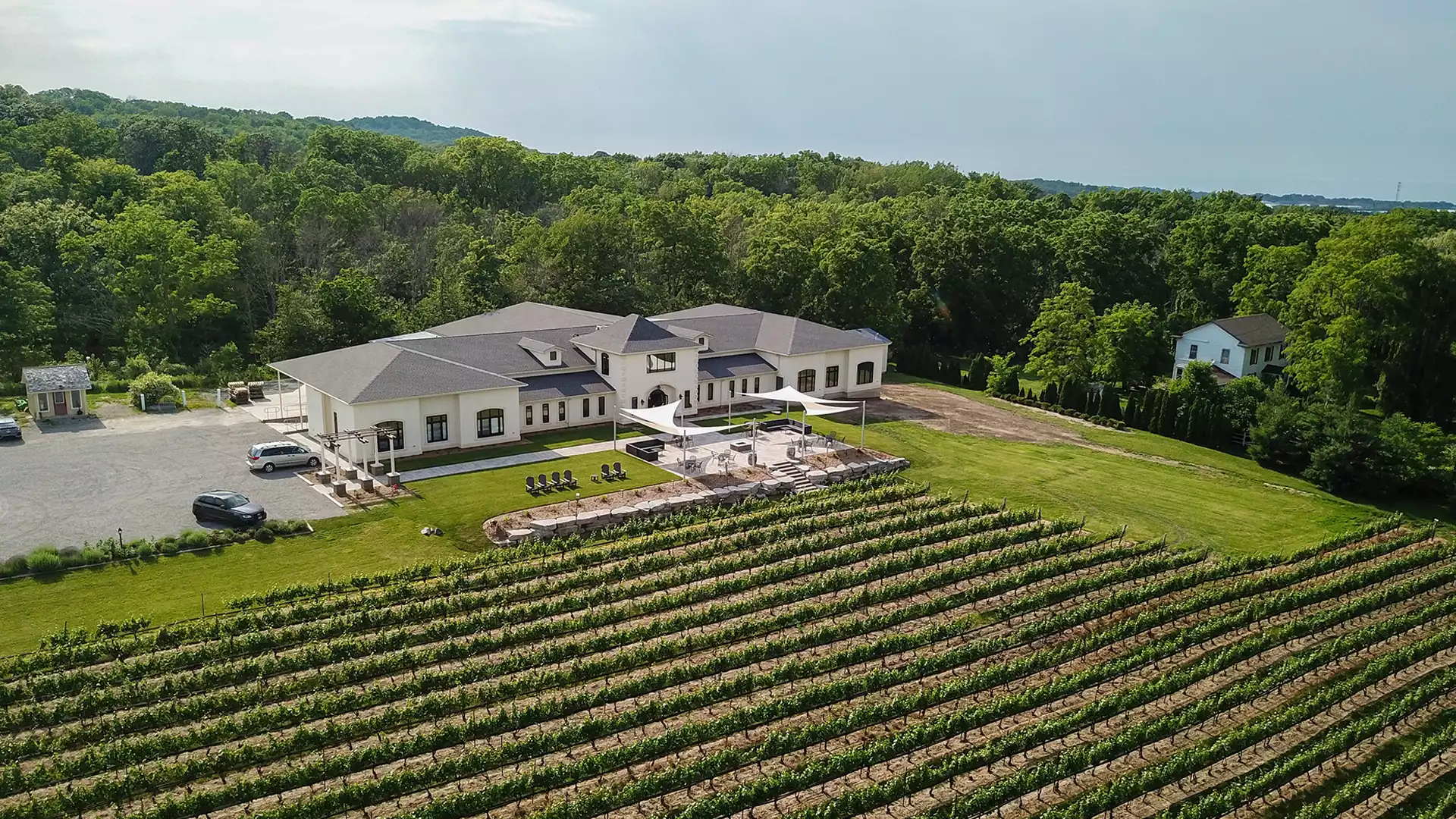 Modern vineyard estate with central building, patio shade sails, and rows of grapevines among rolling hills