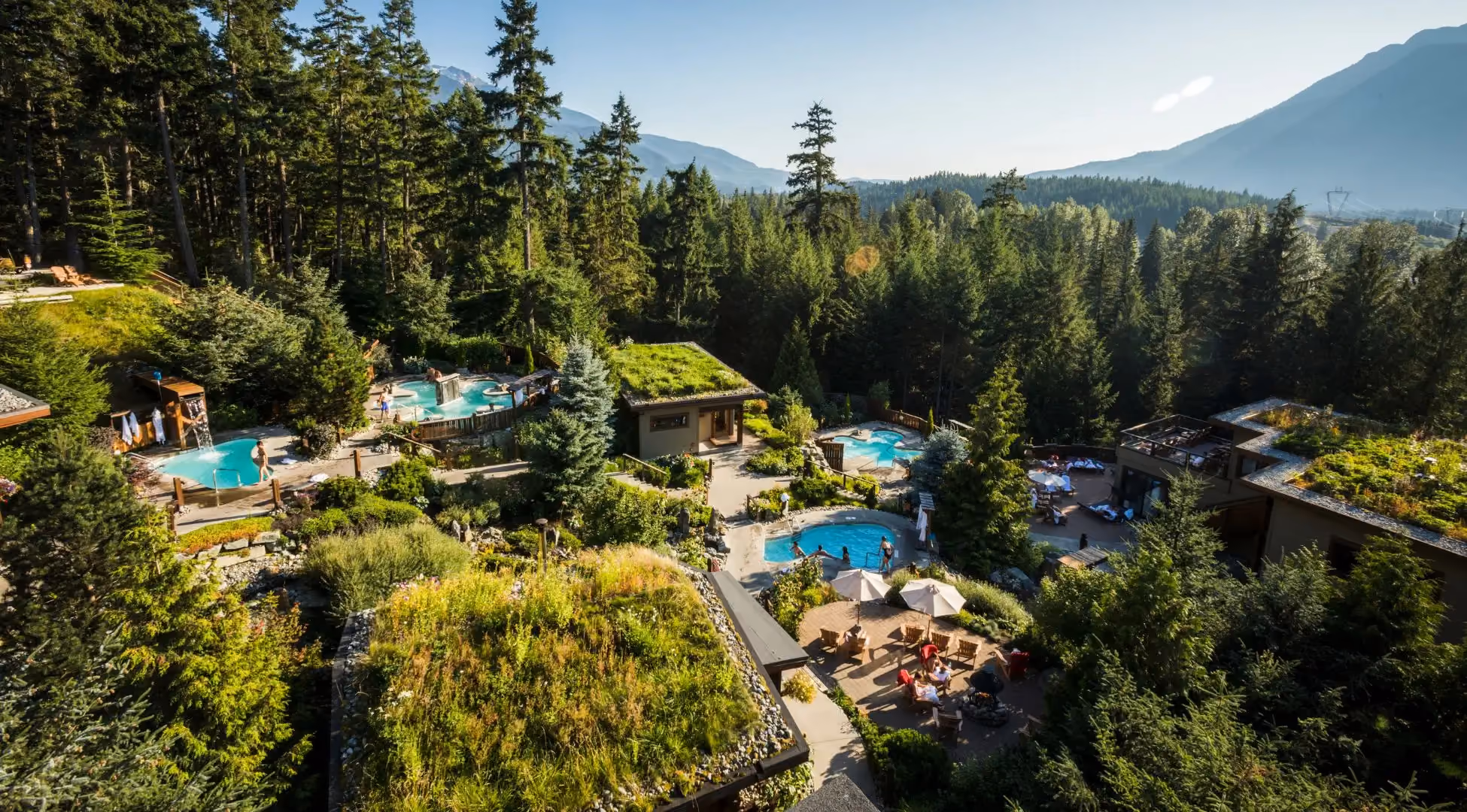 Eco-friendly outdoor spa complex with pools surrounded by forested mountains and green-roof buildings