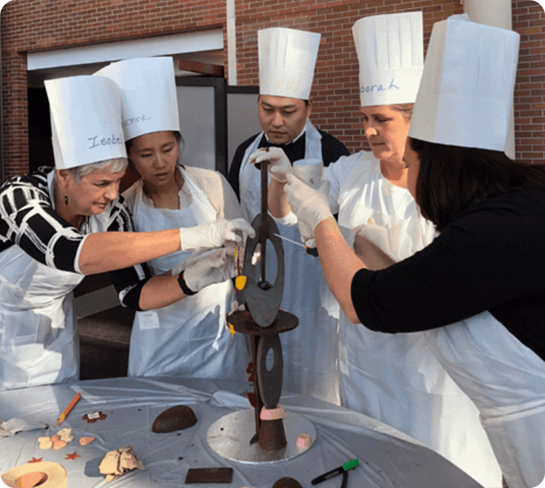 Group of chefs in hats and aprons collaboratively building tall chocolate sculpture