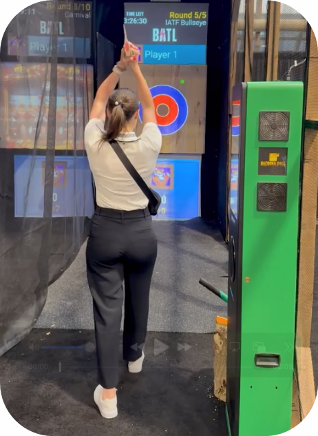 Person preparing to throw axe at wooden target with digital scoreboard overhead
