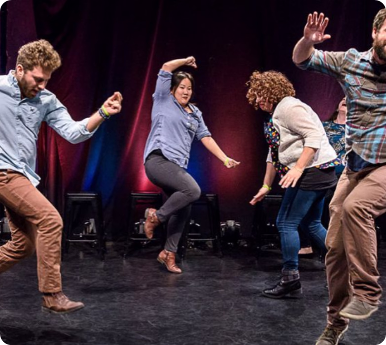 Four dancers performing energetically on stage with red and blue lights