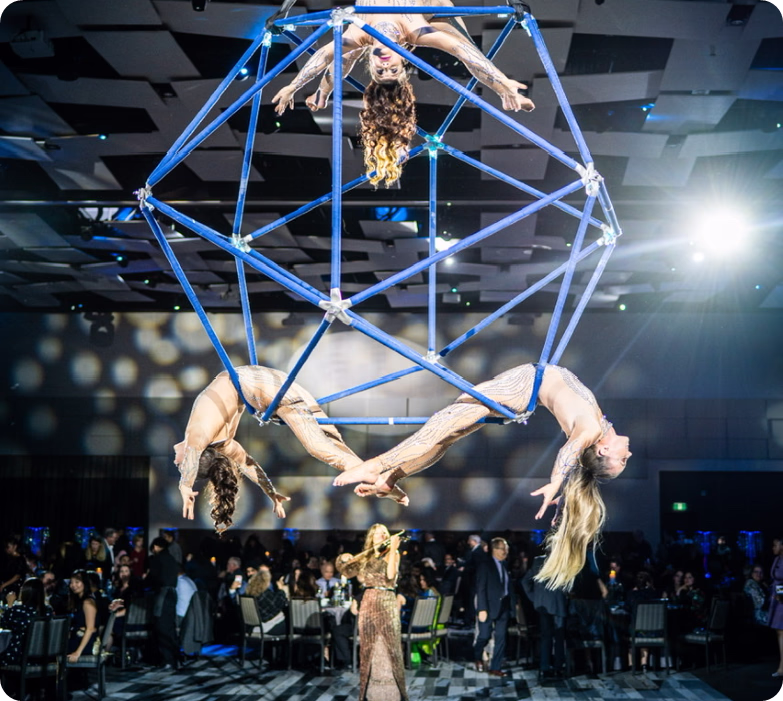 Acrobats suspended in blue geometric frame performing at gala with audience watching