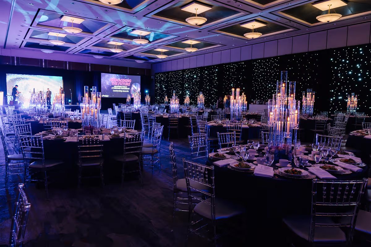 Banquet hall with round tables, candle centerpieces, transparent chairs, and stage displaying Leadership Awards