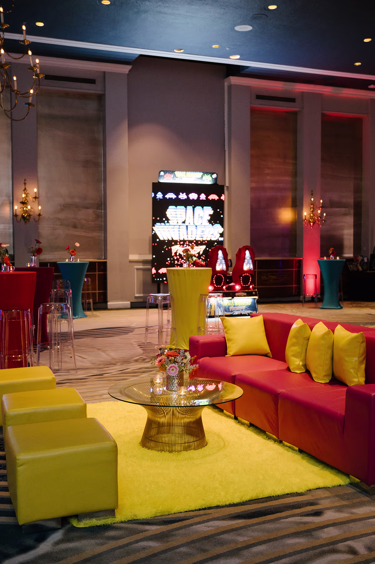 Stylish lounge with colorful furniture, retro Space Invaders arcade machine, and cocktail tables with floral decor