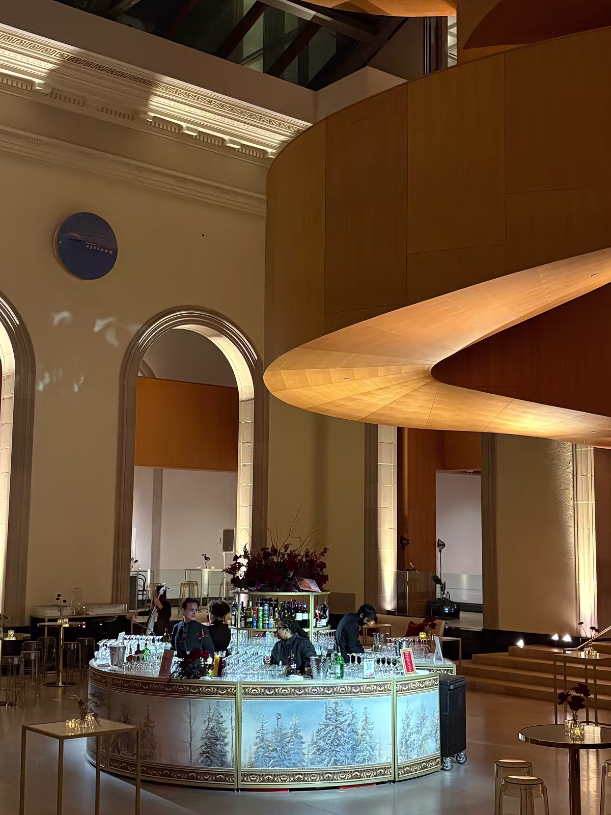 Circular bar with winter-themed artwork, staff arranging glasses, and dramatic wooden architectural structure overhead