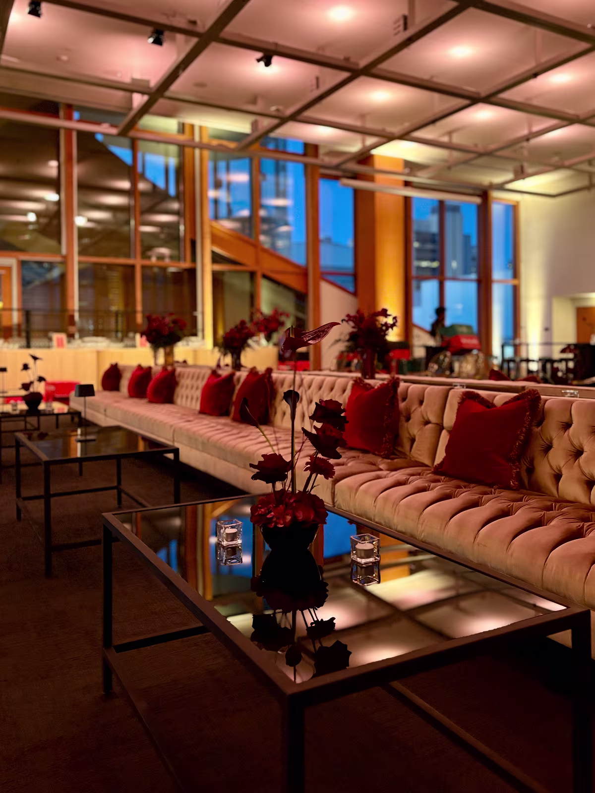 Modern lounge with tufted beige sofa, red pillows, glass tables, and warm ambient lighting