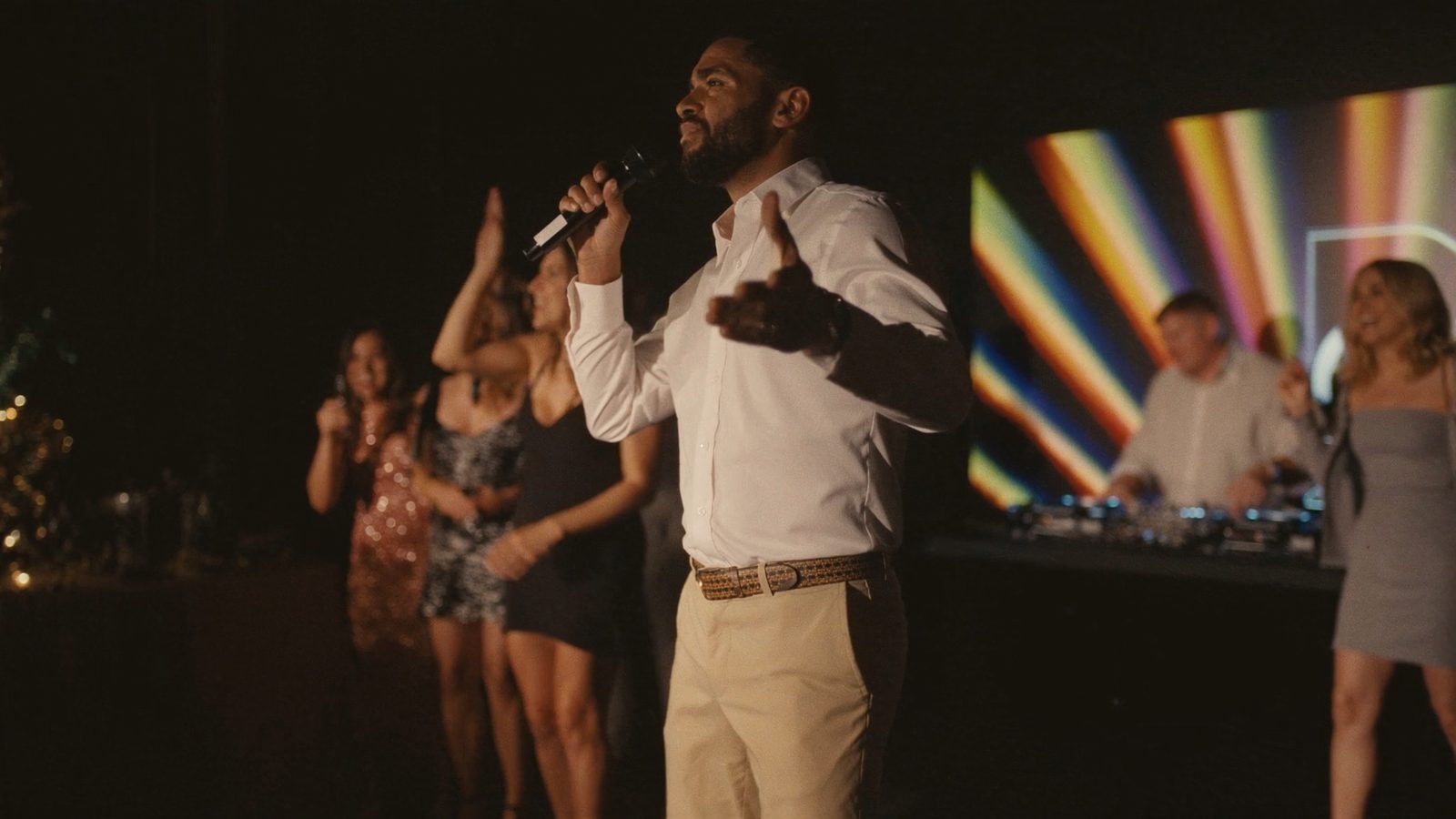 Guest singing karaoke on stage with a DJ booth beside them at a corporate holiday party