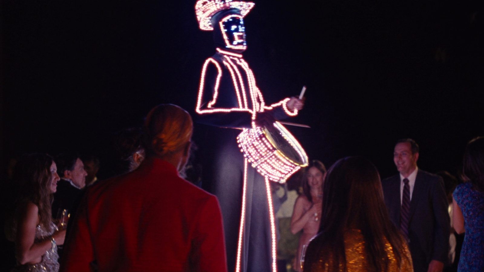Stilt performer in a glowing LED costume playing an LED drum above the crowd