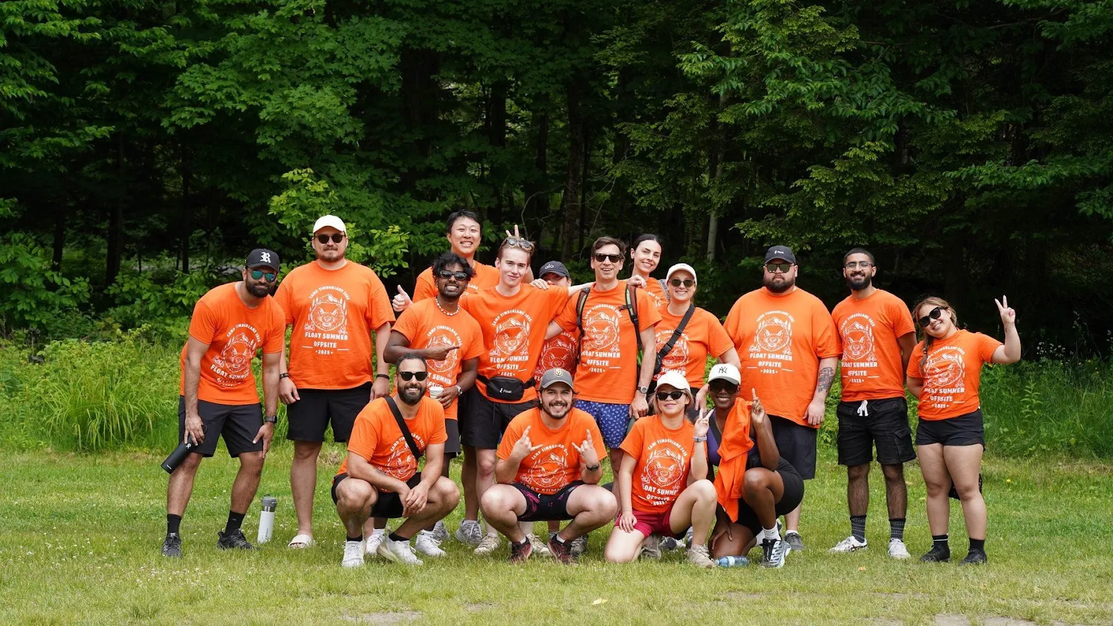 A corporate team in matching orange retreat T-shirts poses for a group photo at a summer camp retreat in Haliburton, Ontario.