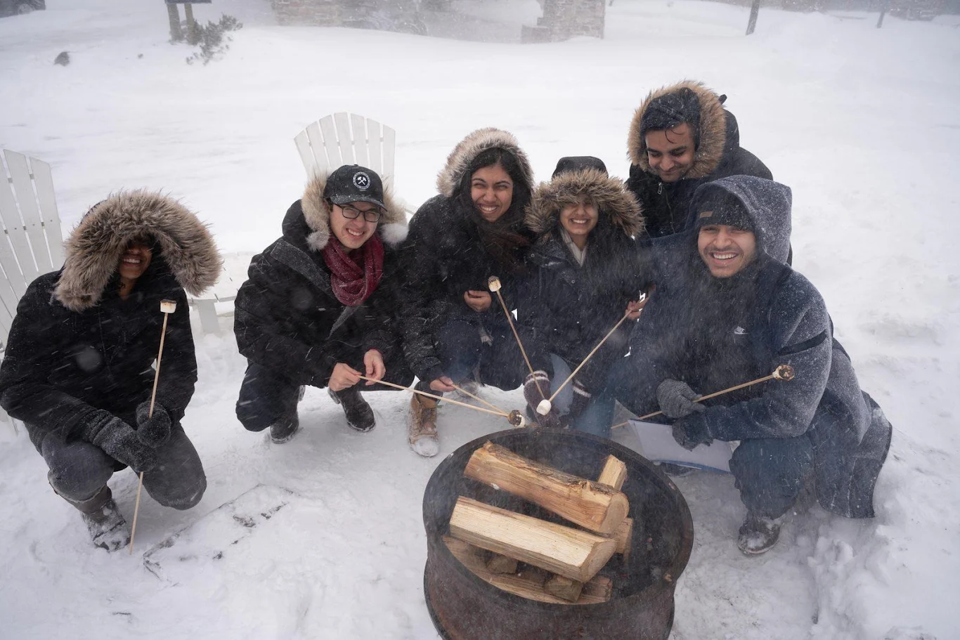Colleagues in winter parkas roast marshmallows around a fire pit during a winter retreat in Muskoka.