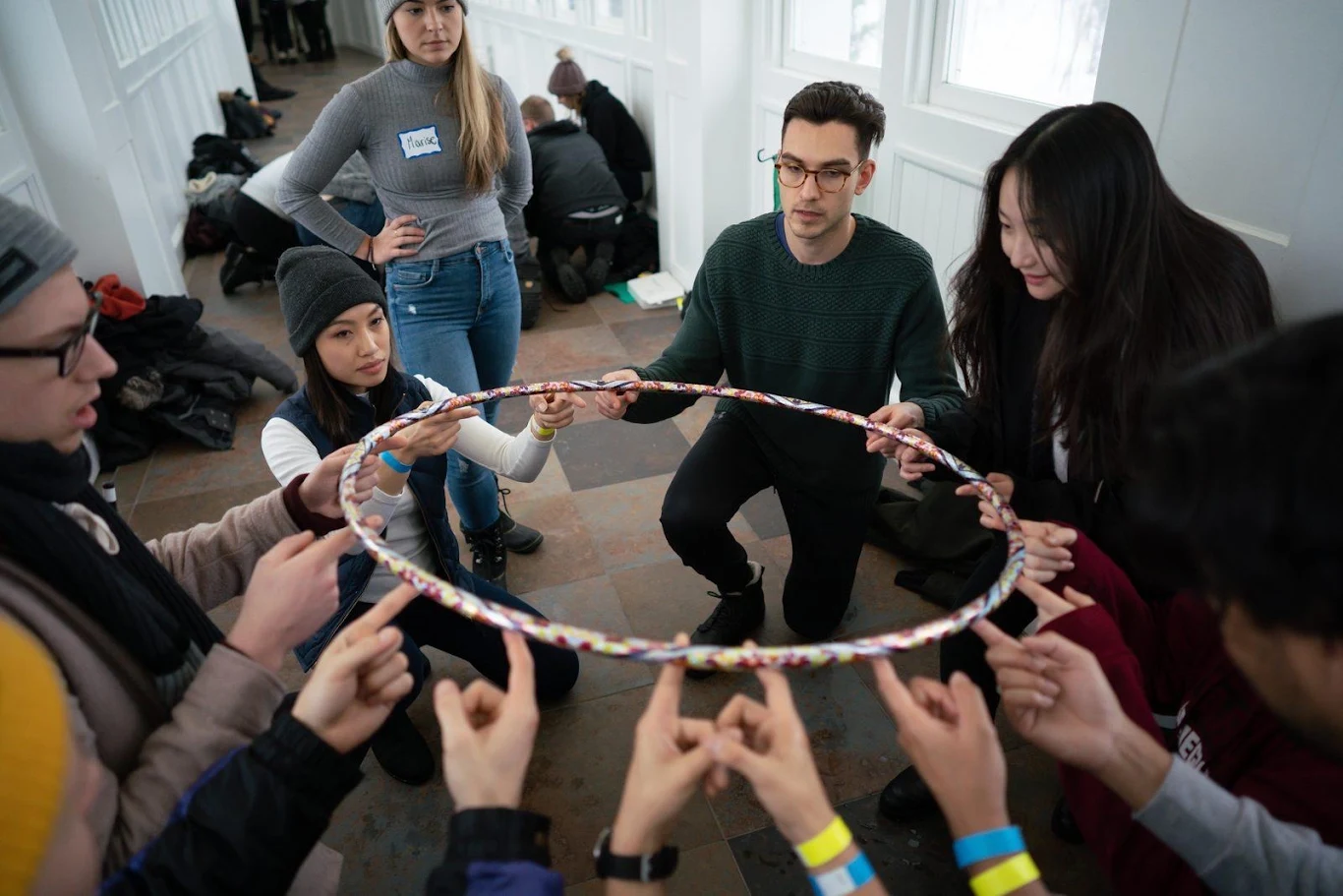 Retreat attendees balance a hoop on their fingertips and work to lower it together in a team challenge.
