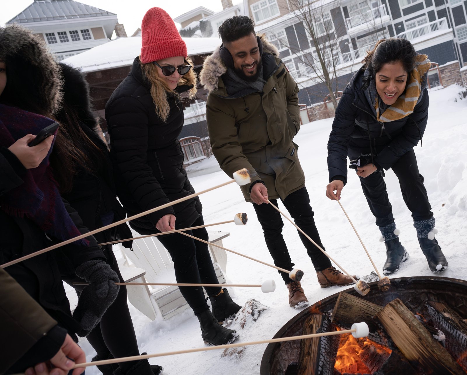 Colleagues in winter coats toast marshmallows over a fire pit in the snow