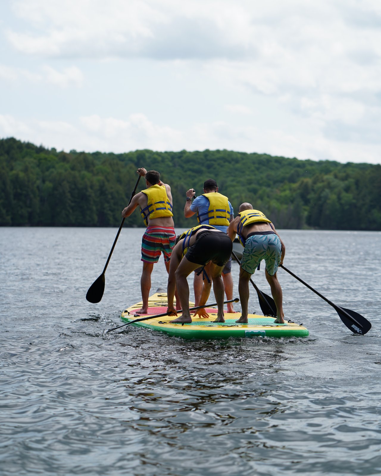 Colleagues in life jackets paddle a large stand-up paddleboard together on a lake