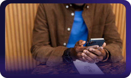 Person wearing a brown jacket and blue shirt holding and using a smartphone at a table.