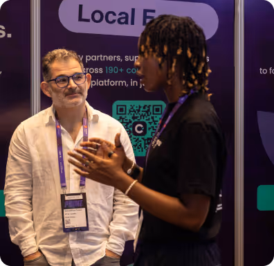 Two men engaging in conversation at a conference booth with a QR code and text in the background.
