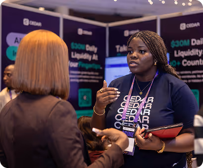 Two women engaged in conversation at a Cedar-branded booth with promotional banners in the background.