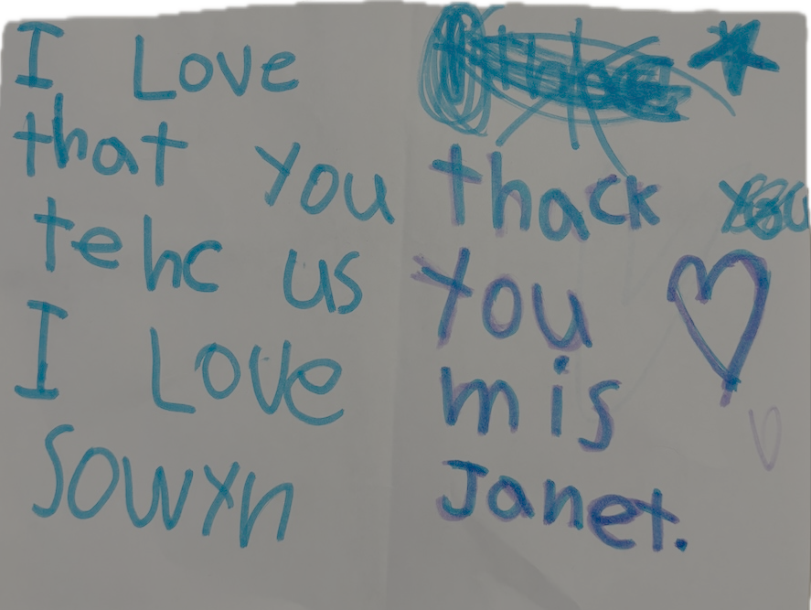 Handwritten note in blue marker reading, 'I love that you teach us. I love you Miss Janet,' with some scribbles and a heart.