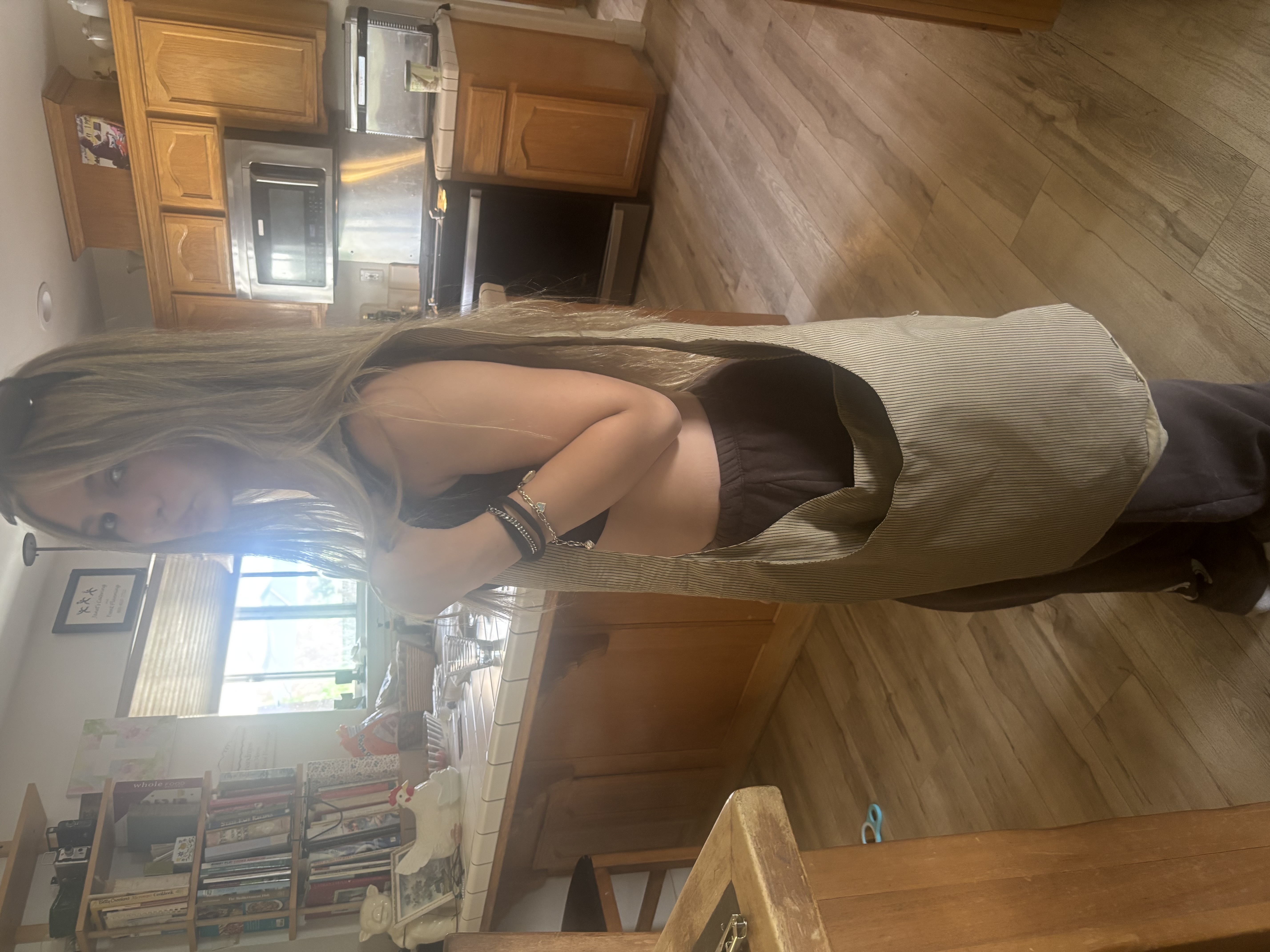 Young woman with long hair holding a large beige shoulder bag in a kitchen with wooden cabinets.