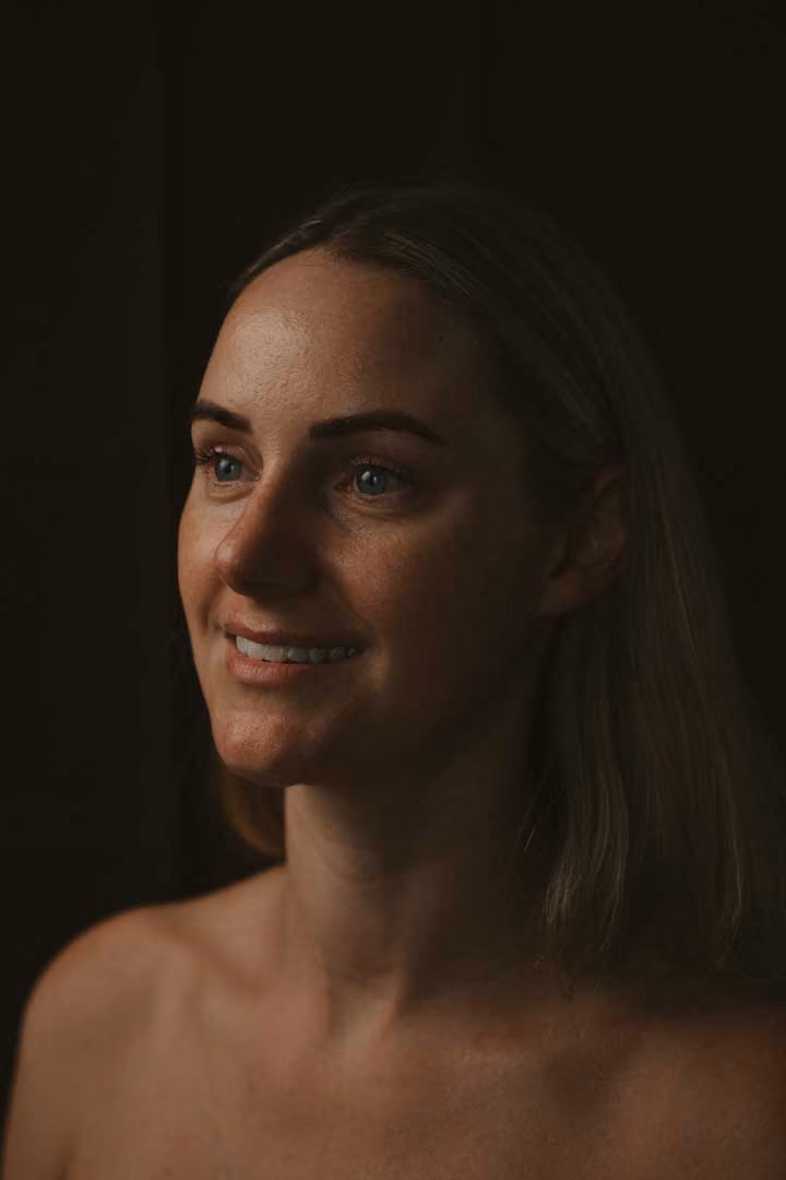 Smiling person looking to the side against a dark background.