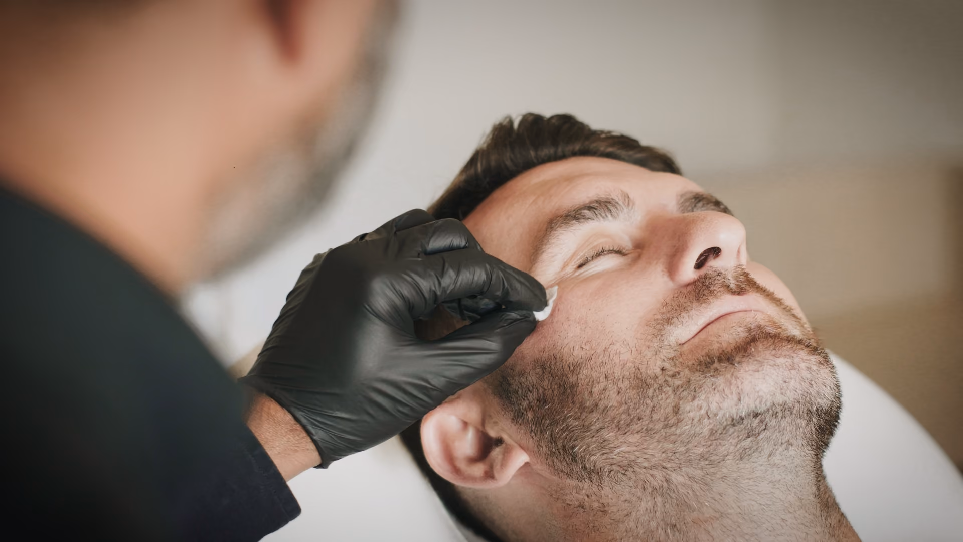 Close-up of clinician performing a non-surgical facial aesthetic treatment on a male patient in a medical clinic.