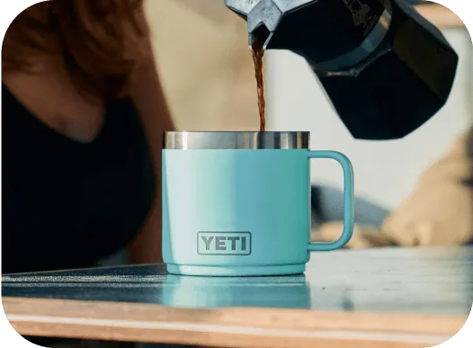 כוס קפה תכלת של YETI על שולחן כשהקפה מוזג ממכשיר איטלקי.