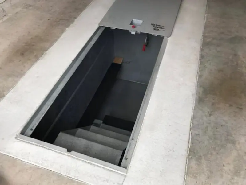 Open hatch revealing concrete stairs leading down to a dimly lit underground space.