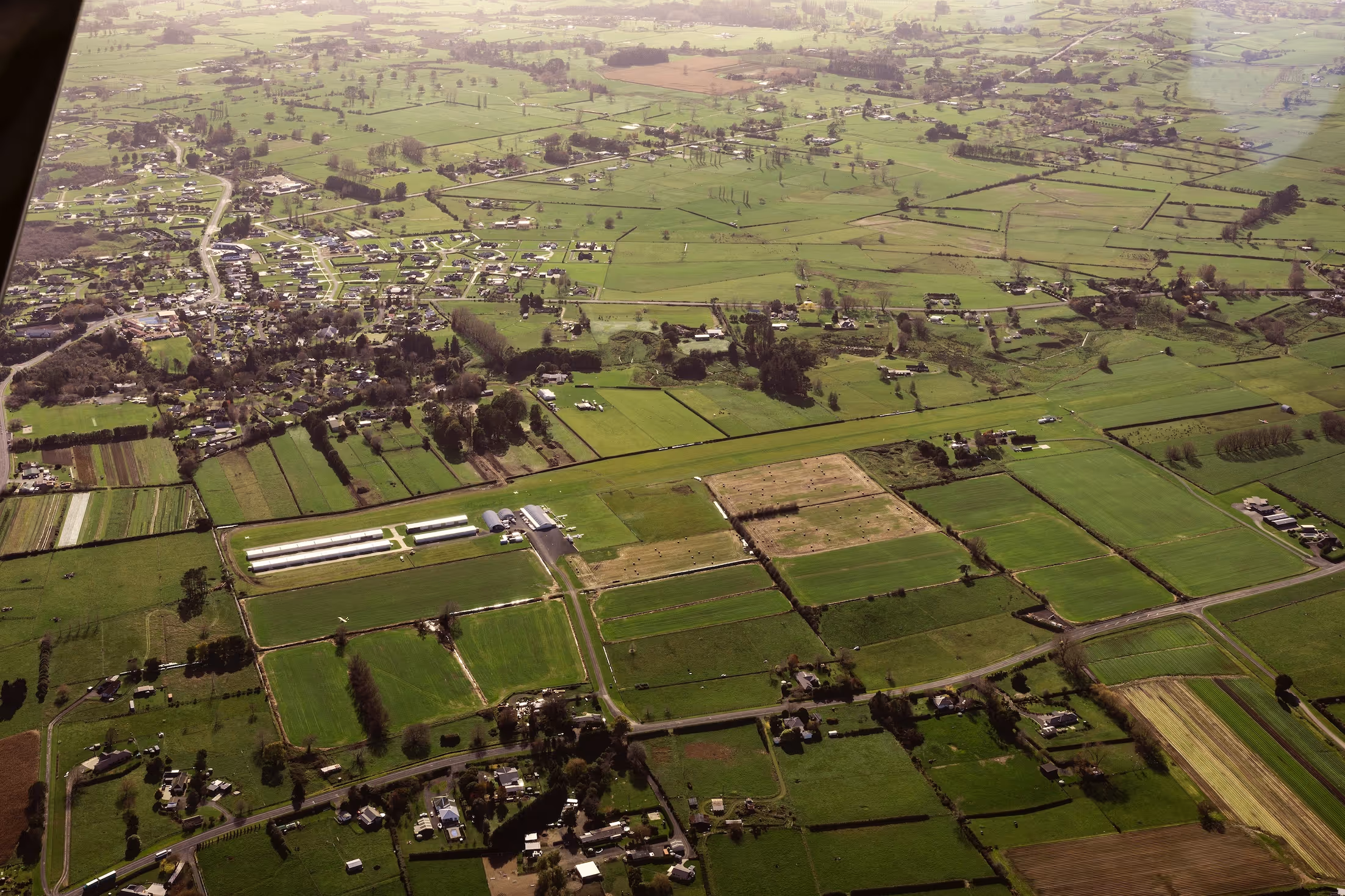 Aerial view of Te Kowhai Airpark, showcasing the lush green landscape and residential areas of the Waikato region. The image highlights the integration of private hangars and homes, emphasising the unique aviation community setting near Hamilton.